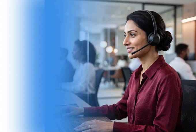 Smiling support agent wearing a headset at her desk in a busy contact centre